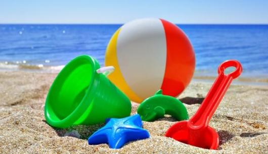 Giocattoli da spiaggia sulla sabbia con mare sullo sfondo.