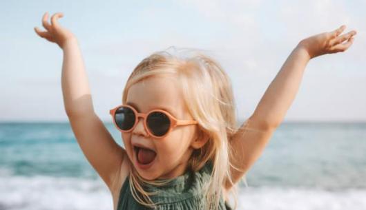 Bambina felice al mare, indossa occhiali da sole arancioni.