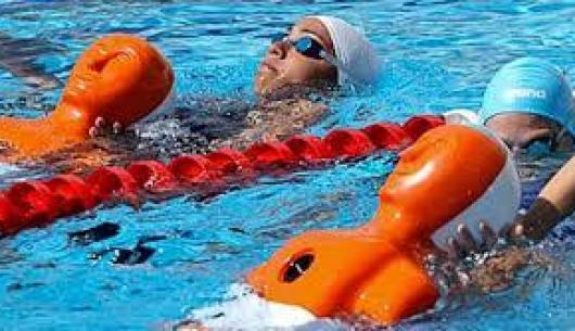 Nuotatori in piscina con manichini arancioni per esercitazioni.